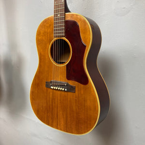 Gibson B-25 Acoustic Guitar Natural 1968 hanging on a wall, showcasing distinctive body checking and vintage craftsmanship.