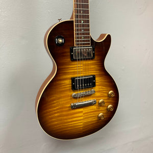 A Gibson Custom Shop Class 5 Les Paul electric guitar with a flame maple top, dual humbuckers, four gold control knobs, and a toggle switch is displayed against a plain light-colored wall.