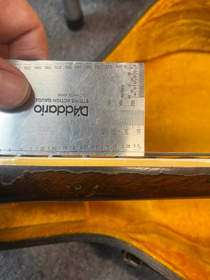 A D'Addario String Action Gauge ruler is held against the frets of a Gibson ES-335TD-12 1968 Sunburst guitar neck, shown inside its yellow-lined case.