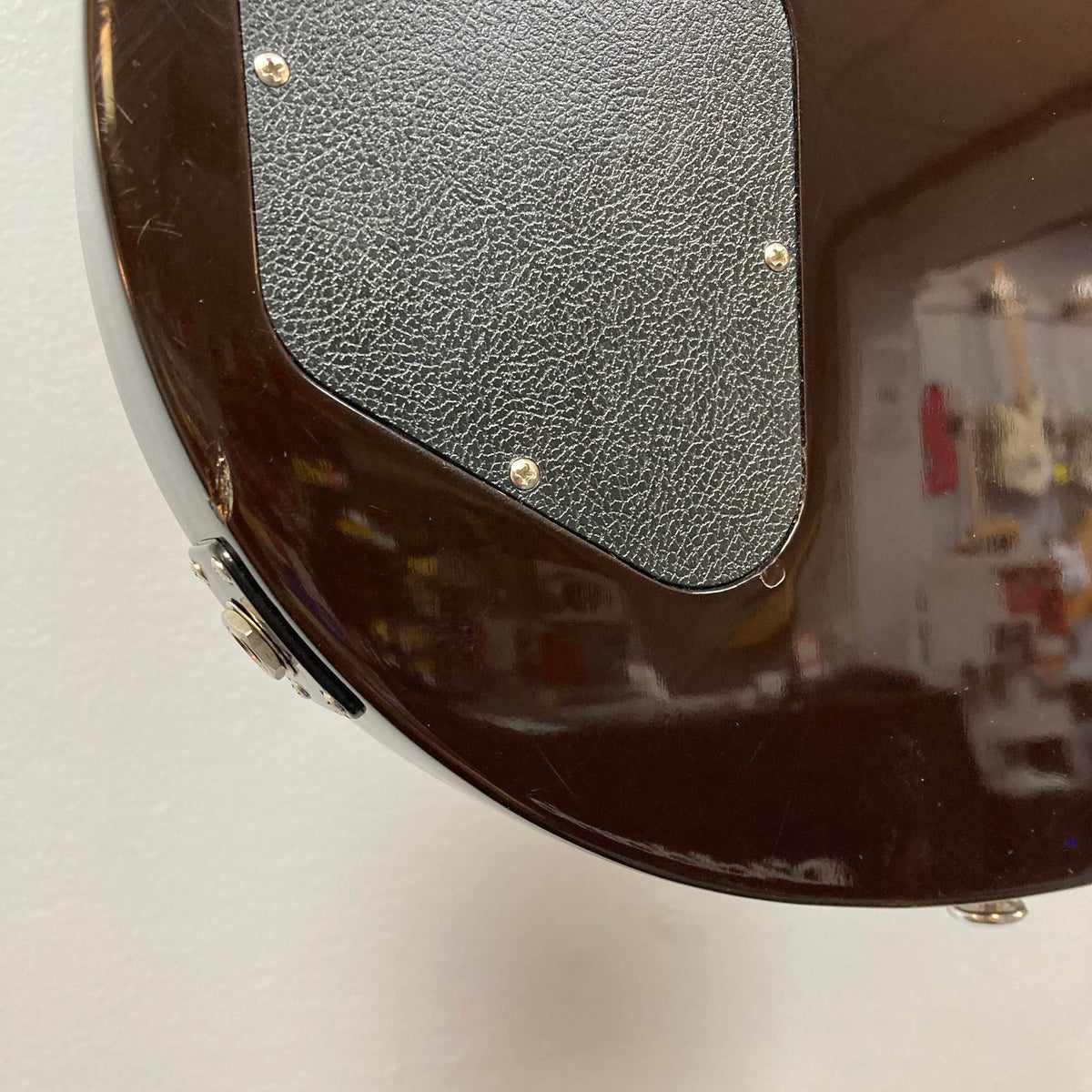 Close-up of the back of a Gibson Les Paul Studio 2015 Desert Burst, featuring a textured black plastic cover plate secured with screws.