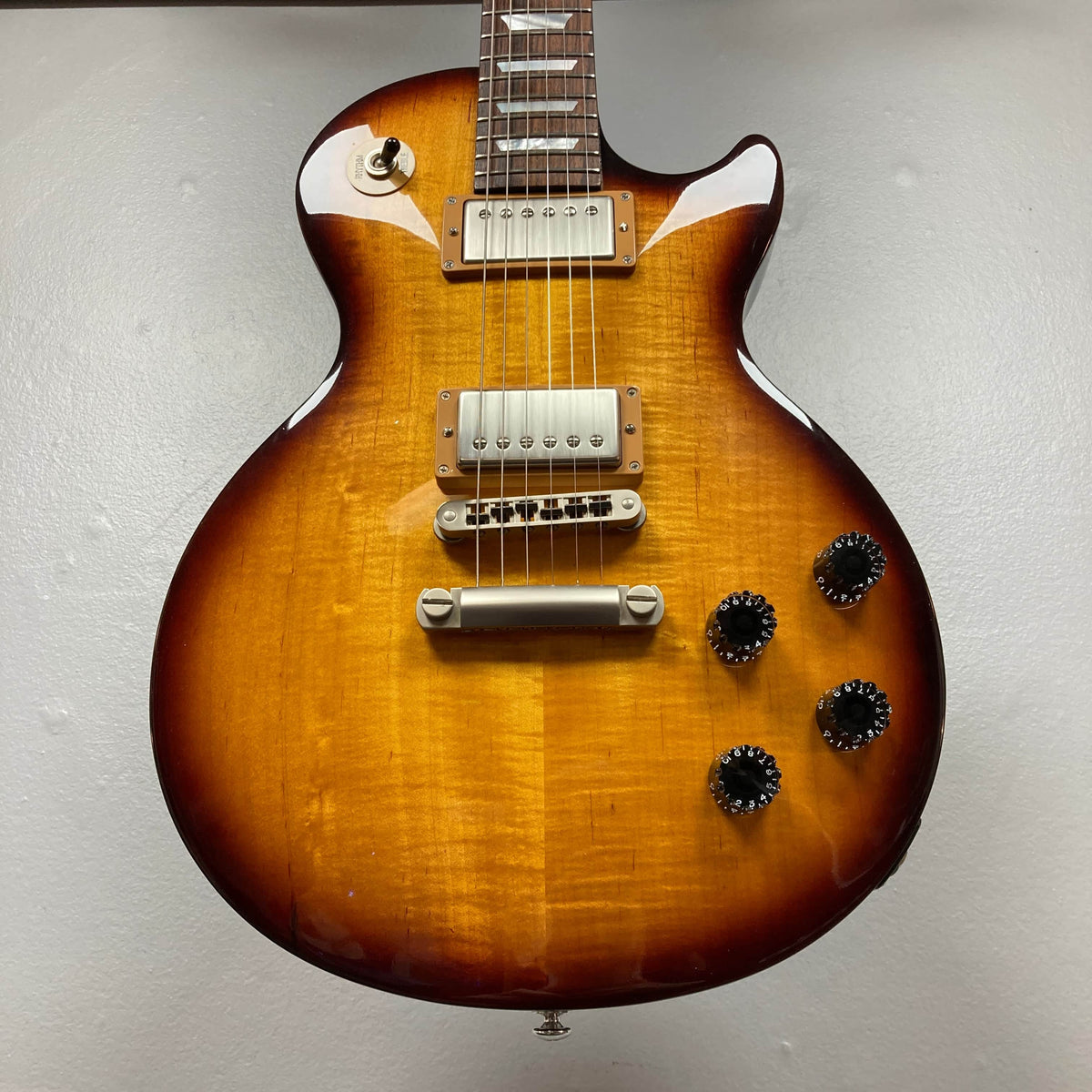 A Gibson Les Paul Studio 2015 Desert Burst electric guitar with two humbuckers, four black knobs, locking tuners, and a toggle switch is shown from the front against a plain wall. Includes case. Brand: Gibson.