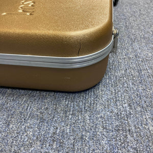 A brown hard-shell case with a cracked corner sits on a blue textured carpet; it once held a Gibson Les Paul Studio 2015 Desert Burst by Gibson, complete with upgraded locking tuners.