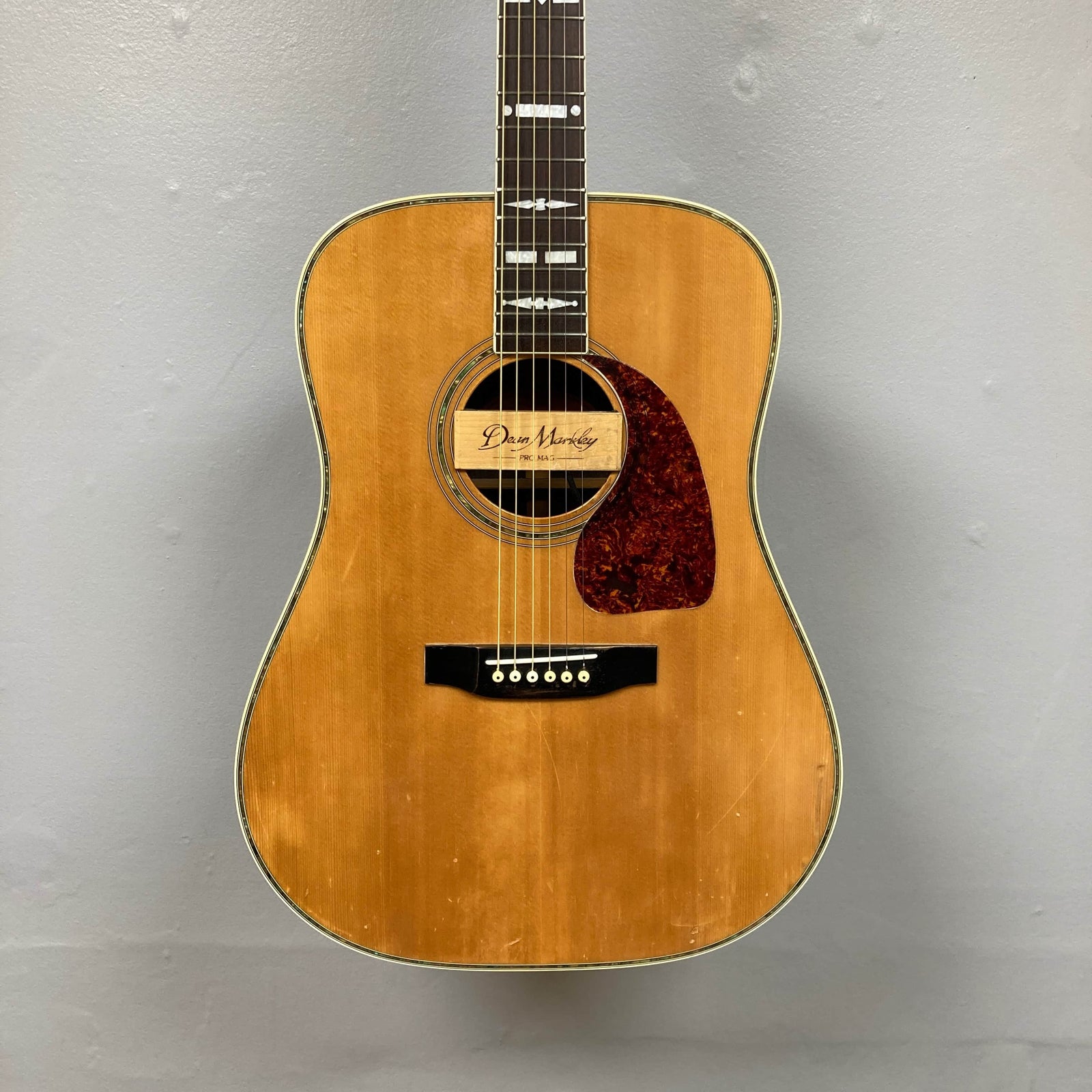 The Gibson Nouveau NV6-R 1986 is a vintage acoustic guitar with a natural wood finish, red pickguard, square shoulder dreadnought shape, and is pictured against a gray background. The Gibson Nouveau NV6-R 1986 is a vintage acoustic guitar with a natural wood finish, red pickguard, square shoulder dreadnought shape, and is pictured against a gray background.