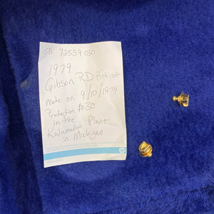 A handwritten note describes a collectible Gibson RD Artist 1977-1982 w/Case by Guitars on Main, shown beside two gold tuning pegs on blue fabric.