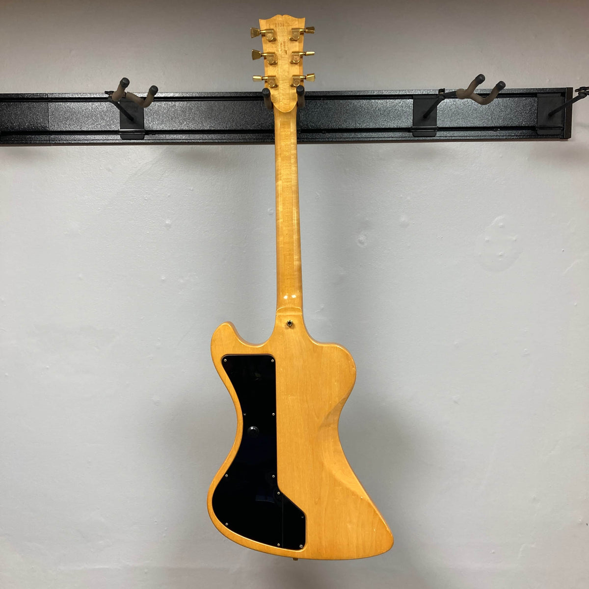 A Gibson RD Artist 1977-1982 from Guitars on Main hangs on a wall-mounted rack, displayed from the back with black plastic covers and gold tuners—a true collectible electric guitar for enthusiasts, includes case.