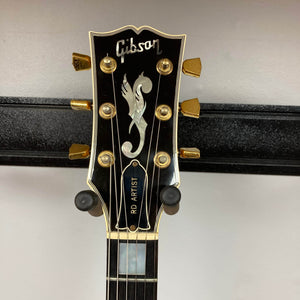 Close-up of a Gibson RD Artist 1977–1982 headstock from Guitars on Main, featuring gold tuning pegs, a decorative inlay, and "RD ARTIST" truss rod cover—a collectible vintage electric guitar w/case.