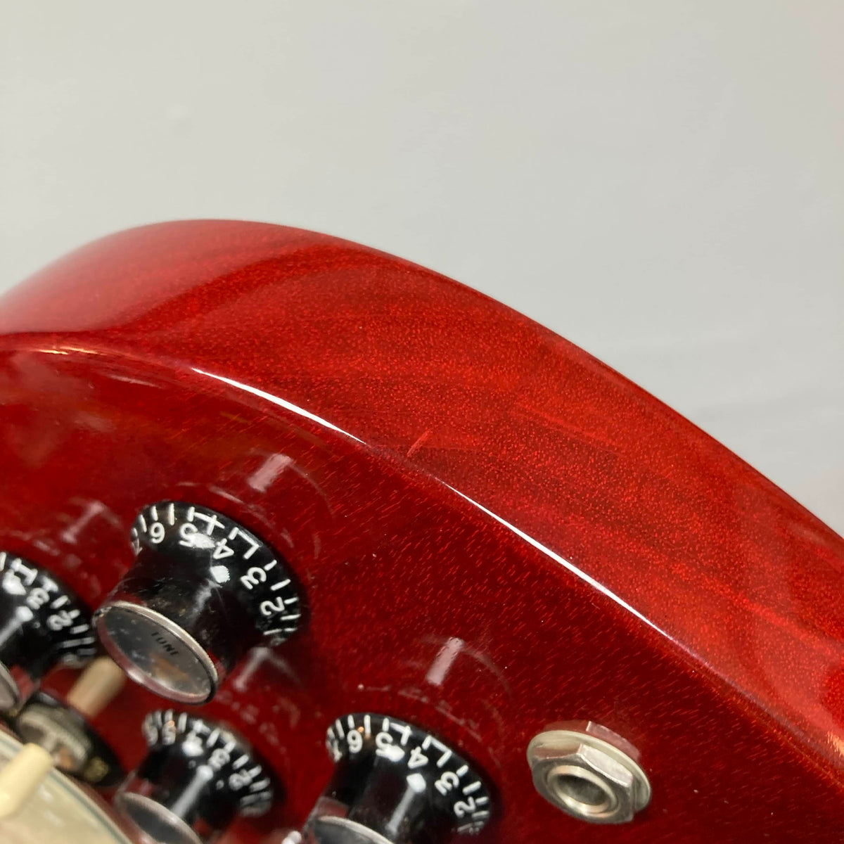 Close-up of a Gibson SG Standard Heritage Cherry yr 2000 Consign, featuring black and silver control knobs and a metal input jack, set against a plain background.