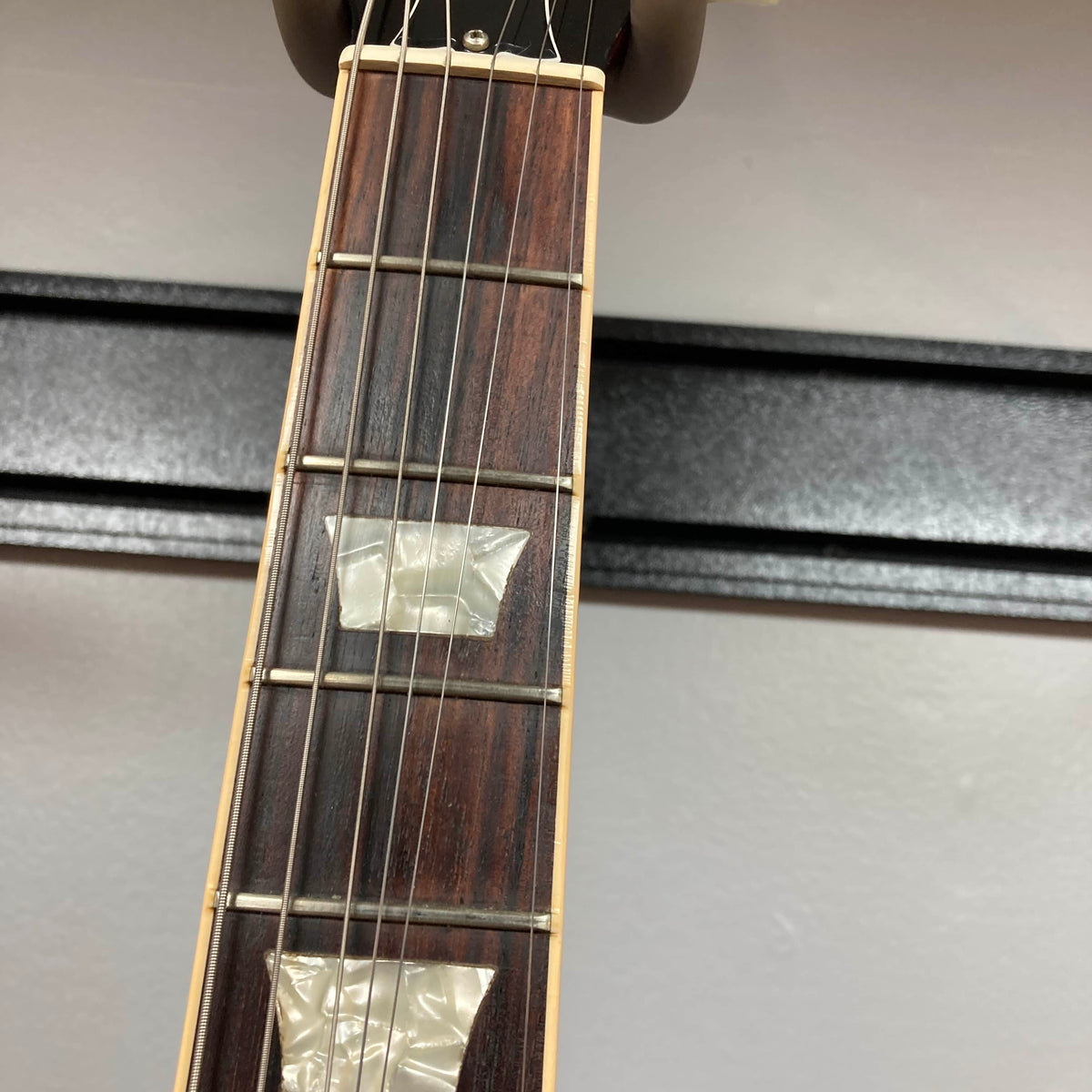 Close-up of a Gibson SG Standard Heritage Cherry yr 2000 Consign guitar neck, featuring six strings, two rectangular mother-of-pearl inlays, and frets set against a light background.