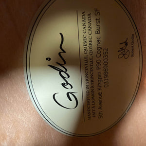 Close-up of the label inside a Godin 5th Avenue Kingpin P90 Cognac Burst SF guitar, displaying the Godin brand, model name, location in Québec, Canada, serial number, and signature—crafted for rich vintage tone.
