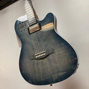 A Godin A6 Ultra Denim Blue Flame SF acoustic electric guitar with a glossy, wood-grain finish hangs on the wall, showing its body, bridge, pickup, and neck. Includes gig bag.