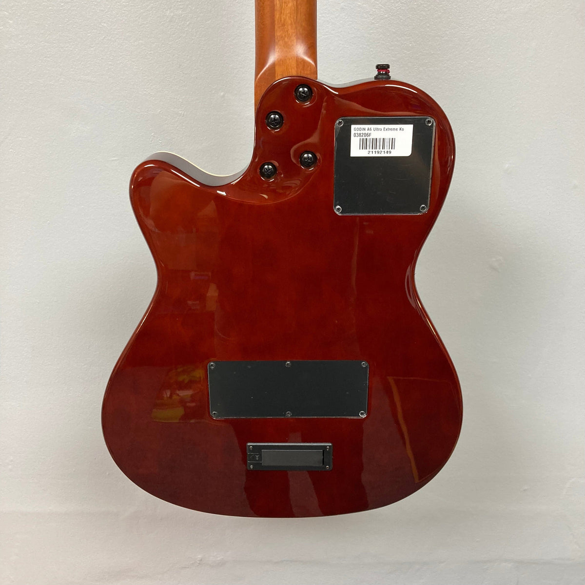 Close-up of Godin A6 Ultra Koa Extreme SF guitar, highlighting strings, neck, and metal plate with barcode.