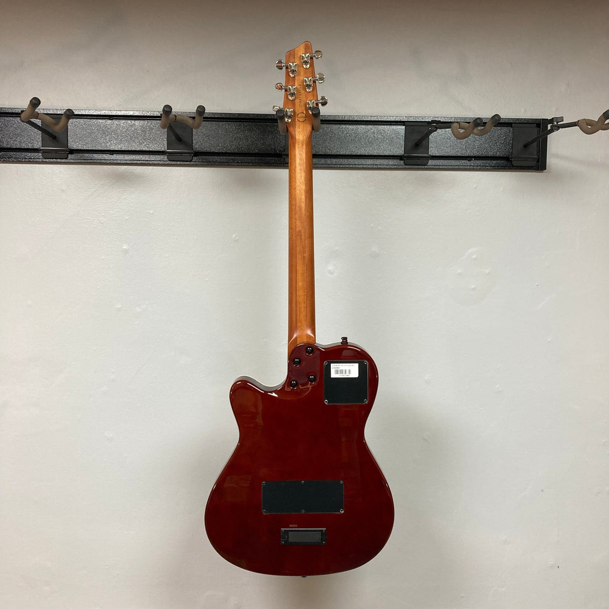 Godin A6 Ultra Koa Extreme SF guitar with visible finish flaw, hanging on a wall.