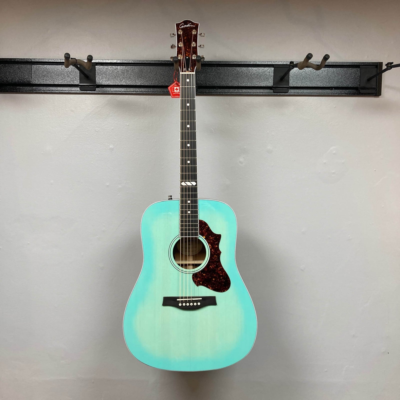 The Godin Imperial Laguna Blue GT EQ SF acoustic guitar with a reddish-brown pickguard, white bridge pins, and simple fretboard design is shown against a plain gray background. Includes gigbag. The Godin Imperial Laguna Blue GT EQ SF acoustic guitar with a reddish-brown pickguard, white bridge pins, and simple fretboard design is shown against a plain gray background. Includes gigbag.