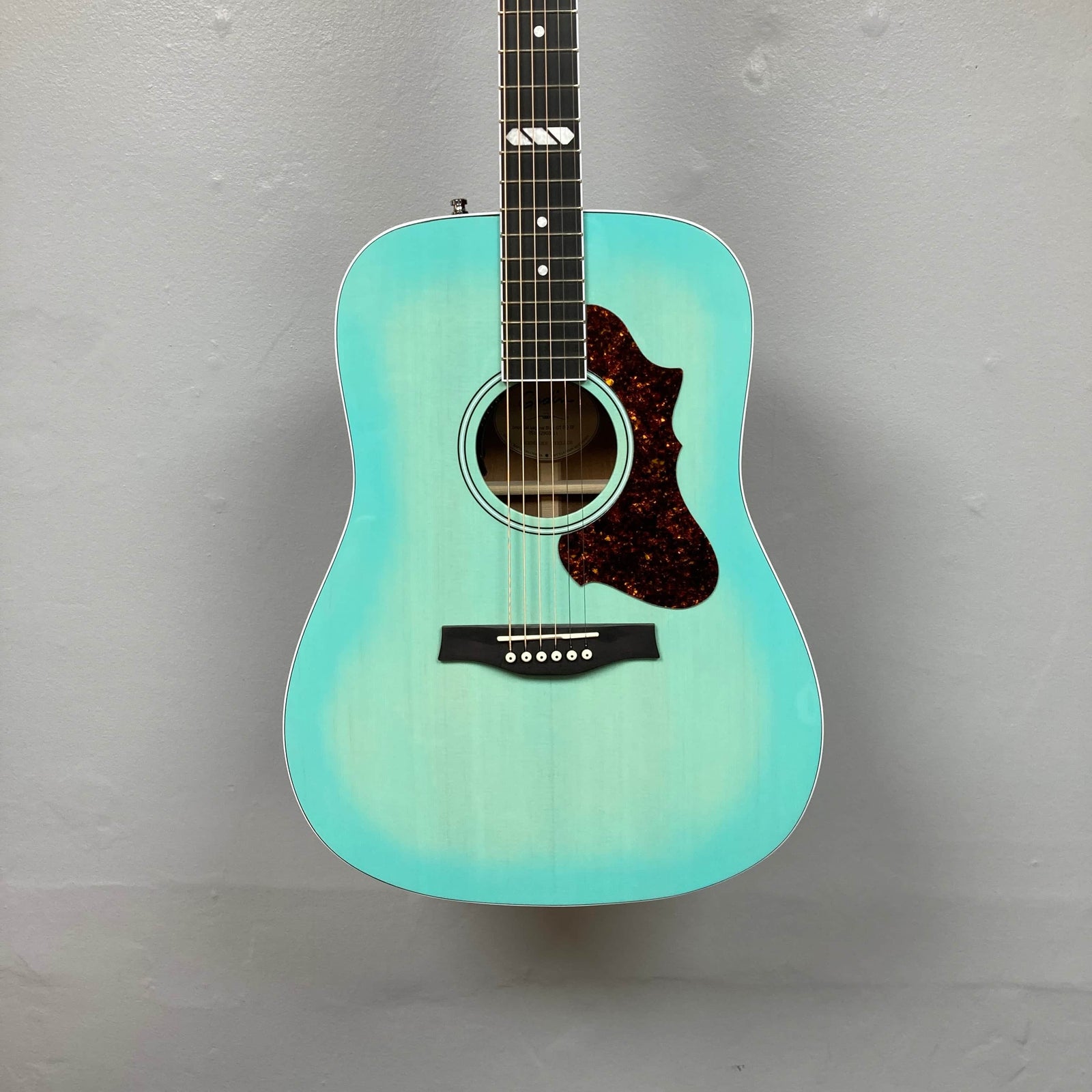 The Godin Imperial Laguna Blue GT EQ SF acoustic guitar with a reddish-brown pickguard, white bridge pins, and simple fretboard design is shown against a plain gray background. Includes gigbag. The Godin Imperial Laguna Blue GT EQ SF acoustic guitar with a reddish-brown pickguard, white bridge pins, and simple fretboard design is shown against a plain gray background. Includes gigbag.