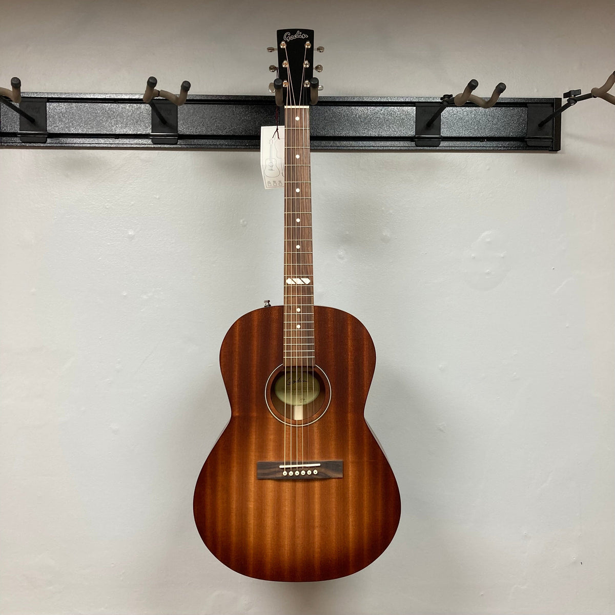 Godin Mahogany Folk Rustic Burst A/E acoustic guitar with solid mahogany body and Fishman Presys VT pickup, displayed on a wall.