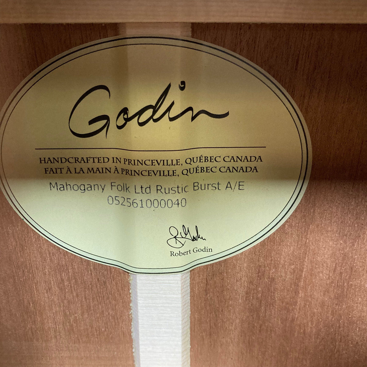 Godin Mahogany Folk Rustic Burst A/E acoustic guitar with a label on a wood surface.