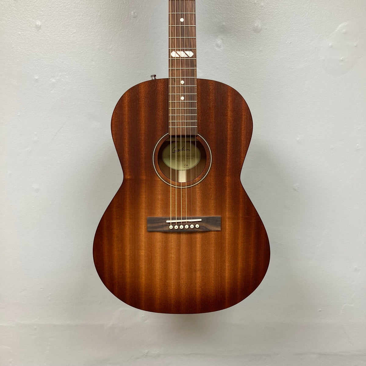Godin Mahogany Folk Rustic Burst A/E acoustic guitar, showcasing its solid mahogany body and strings, mounted on a wall.