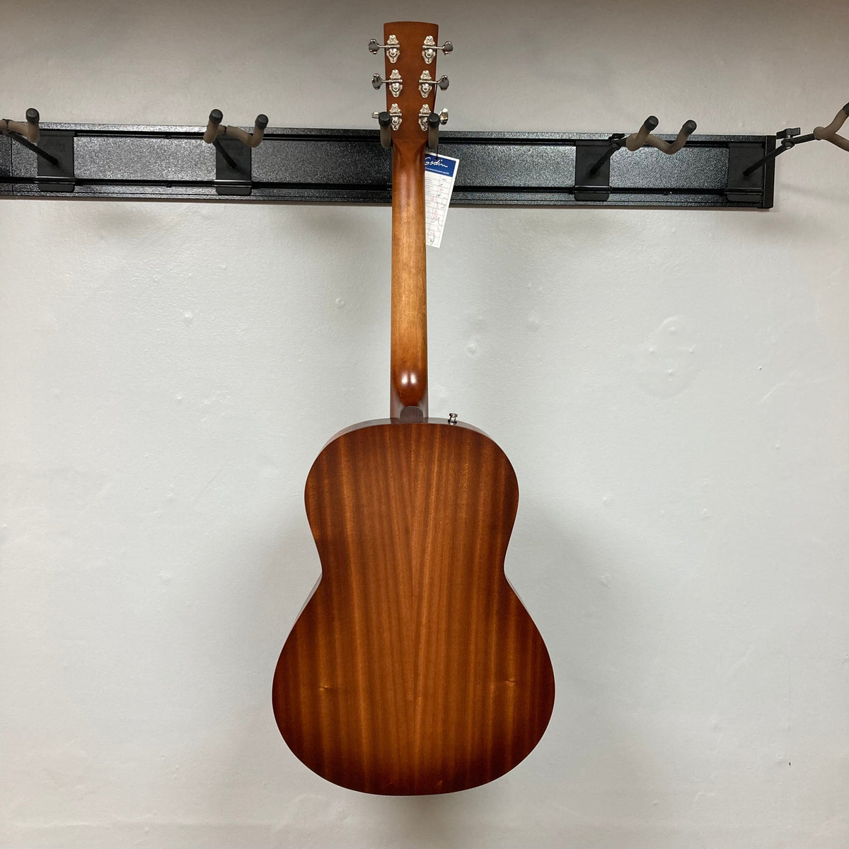 Godin Mahogany Folk Rustic Burst A/E guitar displayed on a wall, showcasing its solid Mahogany build and Fishman Presys VT pickup.