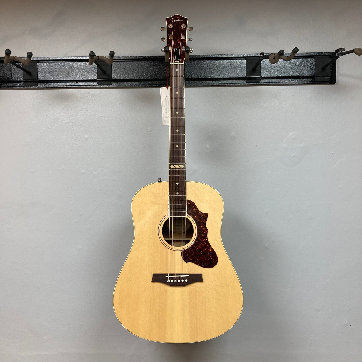 Godin Metropolis Natural RN GT EQ on wall, highlighting its solid spruce top, mahogany back and sides, and rosewood fretboard.