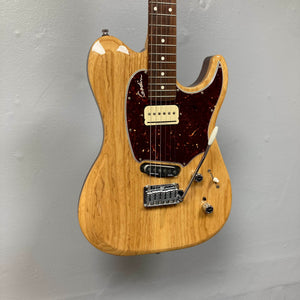 Certainly! Here’s a revised version of the sentence using the provided product data: The Godin Passion Custom Swamp Ash Electric Guitar w/ GigBag Consign by Godin features a natural wood finish, dark pickguard, two pickups—including Seymour Duncan P-Rail pickups for exceptional tonal versatility—and a tremolo bridge, reminiscent of the design and inspiration found in the Godin Passion Swamp Ash Custom. This striking electric guitar is displayed against a plain gray wall.
