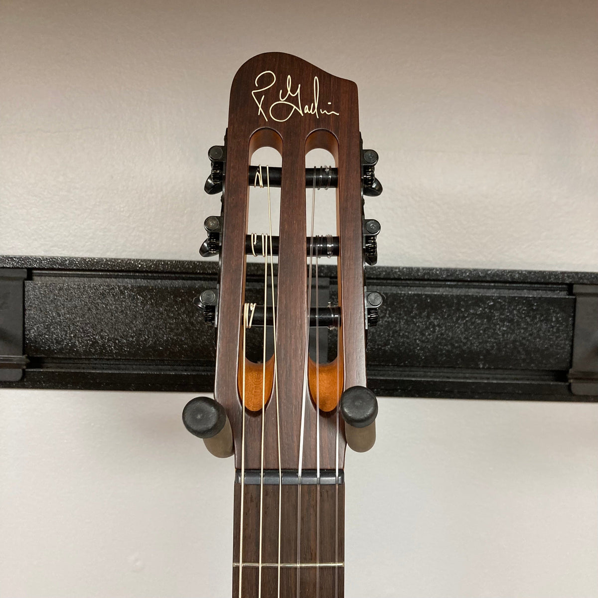 Godin Prototype Ltd Mundial Dark Cedar guitar featuring a close-up of the neck and pegs against a wall, showcasing its craftsmanship and detail.