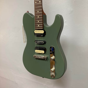 A Godin Radium Matte Green electric guitar with Zebra Humbuckers, tune-o-matic bridge, and chrome knobs hangs against a white wall.