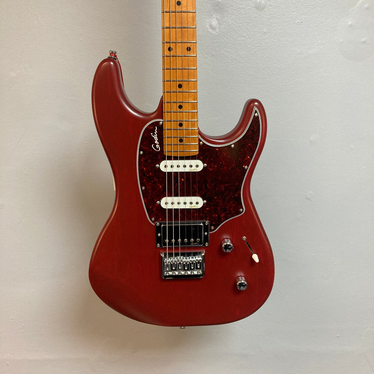 Godin Session HT MN Aztek Red electric guitar with HSS pickup configuration and fixed bridge, mounted on a wall.