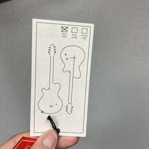 A hand holds a tag with simple line art of electric guitars—evoking the Godin Session T-Pro with Bag by Godin—with checkboxes for "Top," "Back," "Sides," and "Color." Minimalist sketches suggest features like H-S-S pickup configuration.