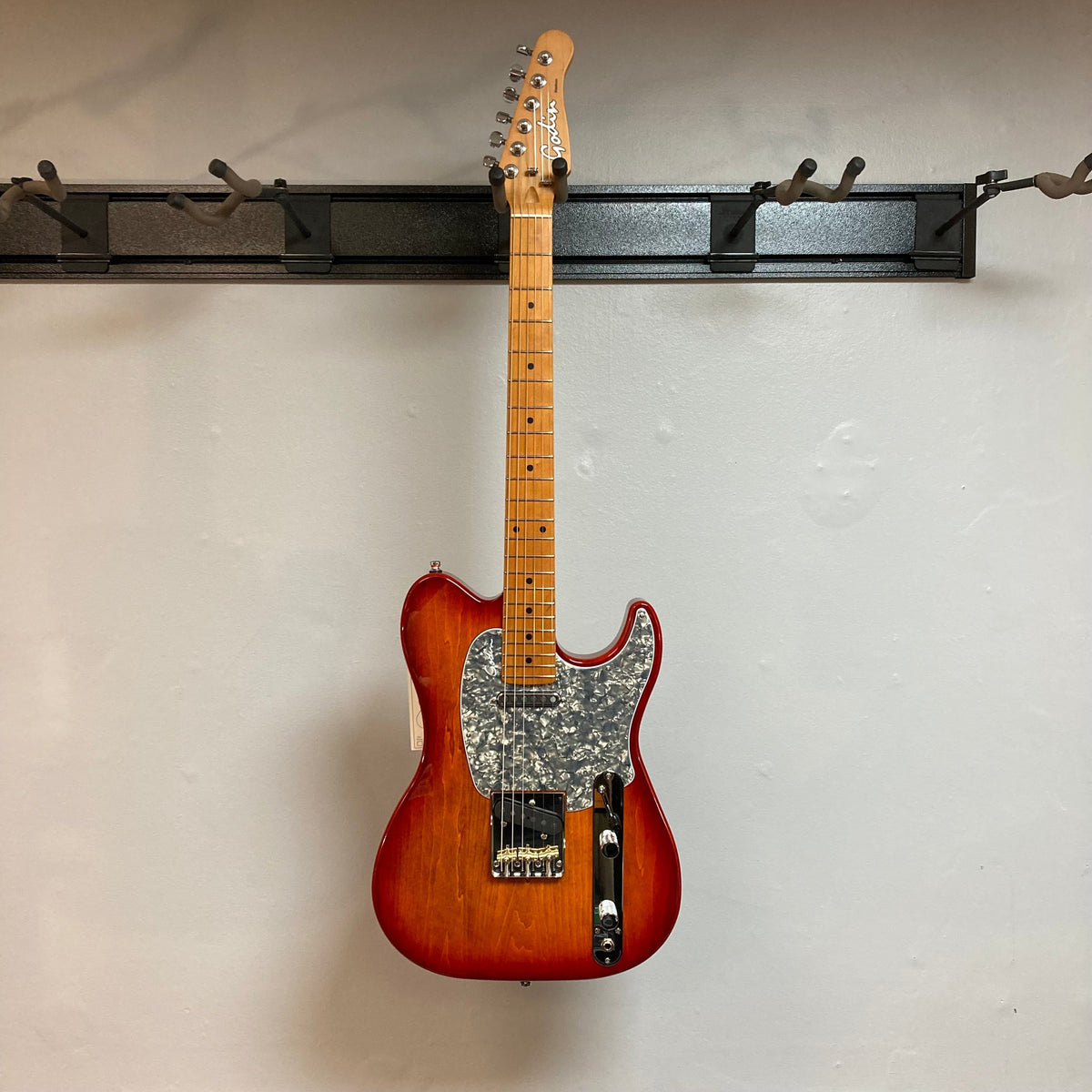 Godin Stadium Pro Sunset Burst MN w/GigBag Electric Guitar on a hook, showcasing neck, strings, and pickups.