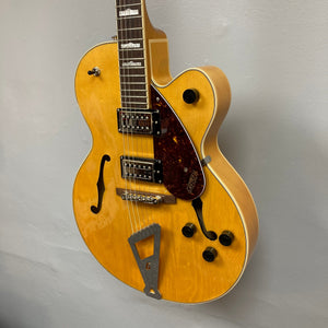 Gretsch G2420 Village Amber Used guitar, showcasing hollowbody design, floating bridge, and Broad'Tron humbuckers, hanging on a wall for display.