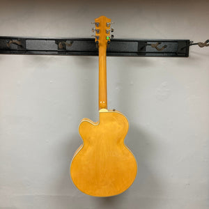 Gretsch G2420 Village Amber Used guitar mounted on a wall, highlighting its hollowbody design and classic Gretsch aesthetic with f-holes and pearloid inlays.