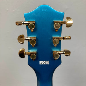 Back of a Riviera Blue Gretsch G2655TG Streamliner Refurb semi-hollow electric guitar headstock featuring six gold tuning pegs and a white sticker with certification symbols.