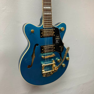 A Gretsch G2655TG Streamliner Riviera Blue Refurb semi-hollow electric guitar with gold hardware, Broad’Tron BT 3S pickups, a Bigsby tremolo, and an f-hole is hanging on a white wall.