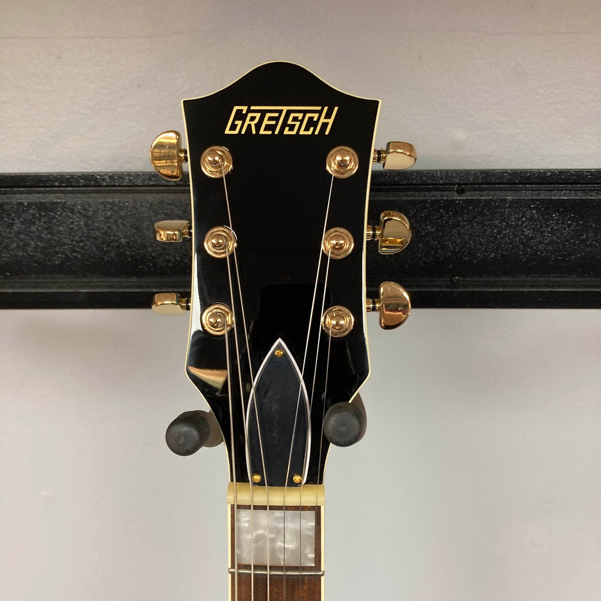Close-up of a Gretsch G2655TG Streamliner Riviera Blue Refurb guitar headstock with gold tuning pegs and the Gretsch logo, set against a plain wall background.
