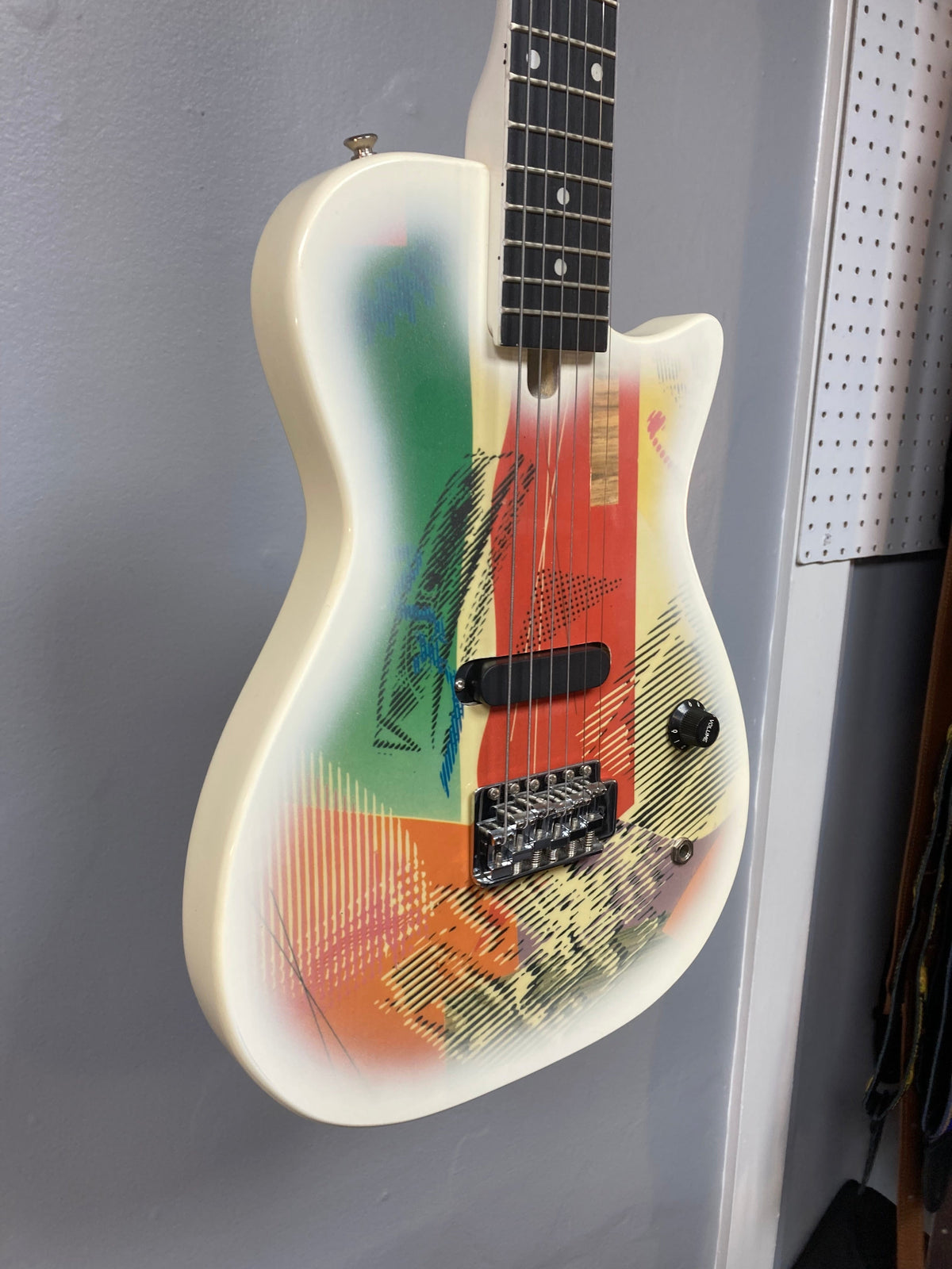 Gretsch Traveling Wilburys TW-100T Electric Guitar, featuring a colorful design and black volume knob, displayed on a wall.