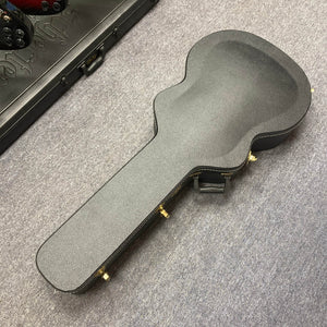 A black Guild USA F-512 w/OHSC 2005 Circa guitar case with gold latches lies on a gray carpeted floor.