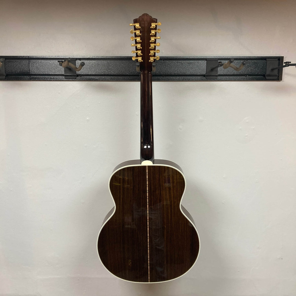 A Guild USA F-512 w/OHSC 2005 Circa 12-string acoustic guitar by Guild hangs on a wall rack, displayed from the back to show its dark wood finish and white binding.