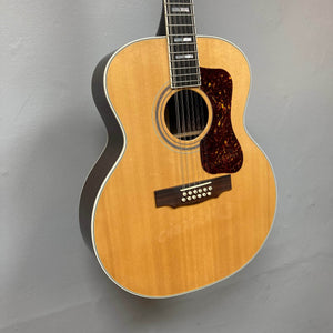 A Guild USA F-512 w/OHSC 2005 Circa 12-string acoustic guitar by Guild with a natural wood finish hangs on a light gray wall.