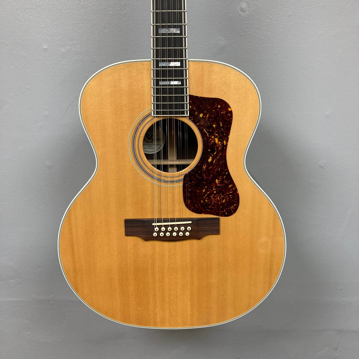 The Guild USA F-512 w/OHSC 2005 Circa 12-string acoustic guitar features a natural finish, tortoiseshell-patterned pickguard, and classic jumbo body—crafted for rich tone and timeless style by Guild.