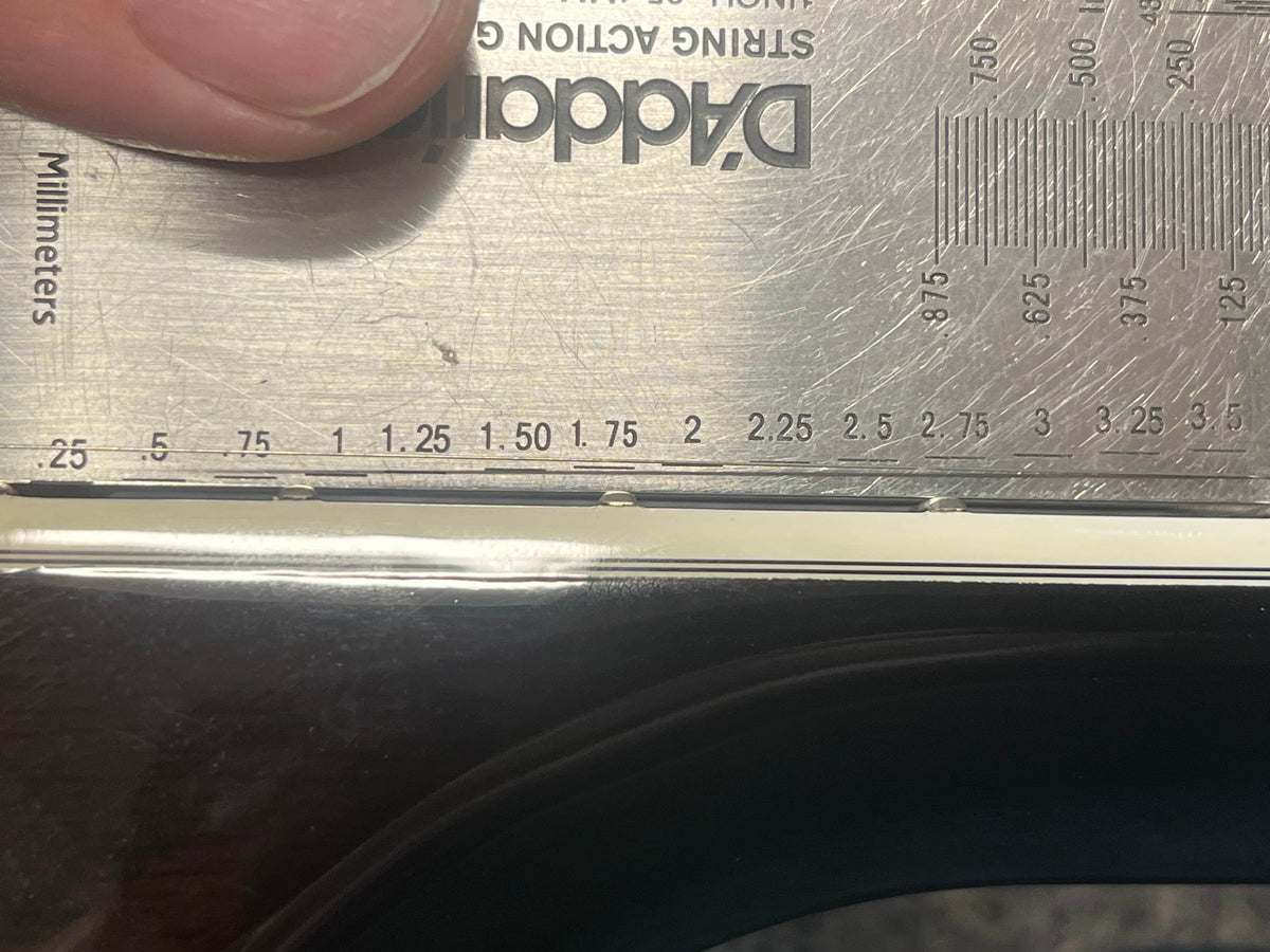 A metal ruler marked in mm and inches measures the width of a Guild USA F-512 w/OHSC 2005 Circa by Guild, showing it's slightly over 2 inches. A hand holds the ruler in place.