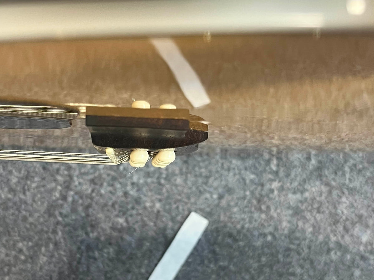 Close-up of the Guild USA F-512 w/OHSC 2005 Circa acoustic guitar bridge with six strings and plastic pins, shot from above on a grey carpet with white tape strips—reflecting classic Guild jumbo 12-string design.