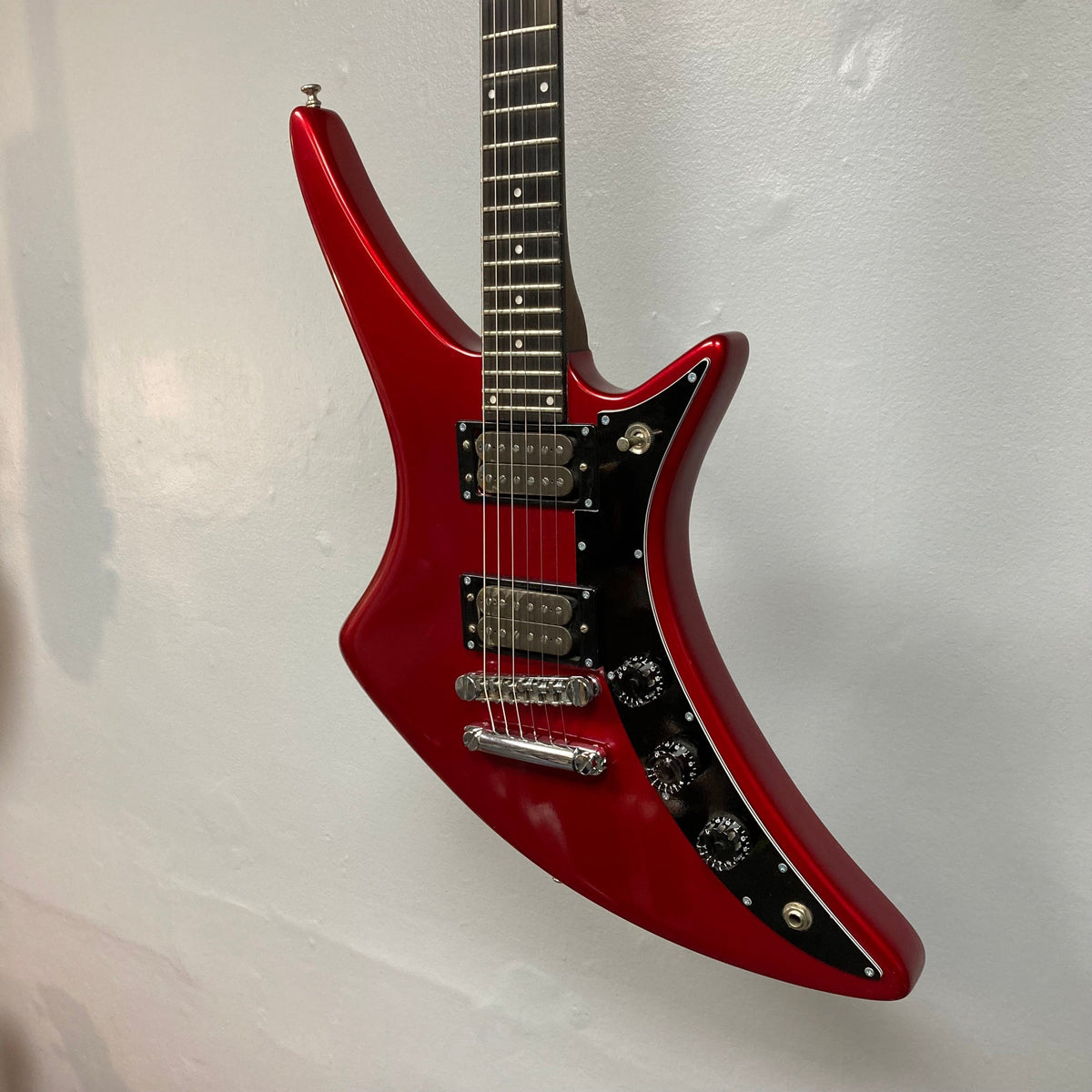 Guild USA X-79 Candy Apple Red electric guitar, featuring a unique body shape and 24-fret fingerboard, displayed on a wall.