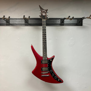 Guild USA X-79 Candy Apple Red electric guitar on a hook, featuring a unique body shape and 24-fret fingerboard, with a case included.