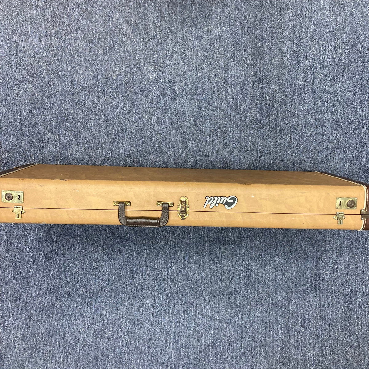Guild USA X-79 Candy Apple Red guitar in a brown wooden case with handle, shown on a carpet.