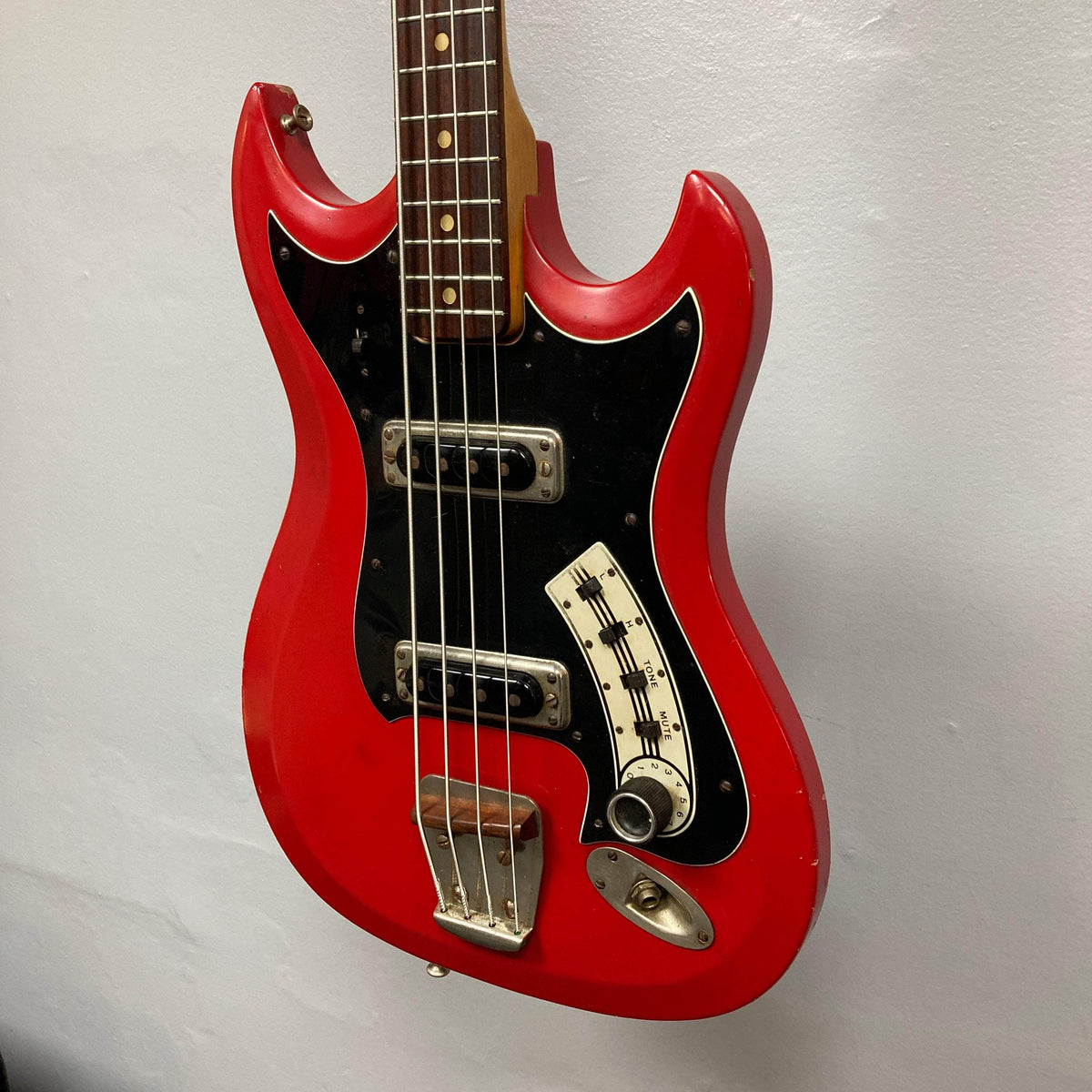 Hagstrom HII-B Mid-1960s Red Medium-Scale Bass with black pickguard, dual pickups, chrome bridge, leaning against a wall, showcasing vintage Scandinavian design.