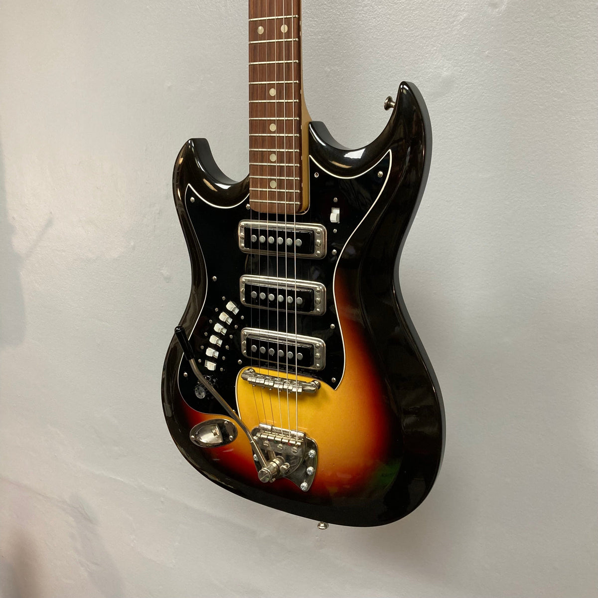 Hagstrom III Left Hand 1960s Sunburst Electric Guitar on wall, showcasing its vintage design and three single-coil pickups.