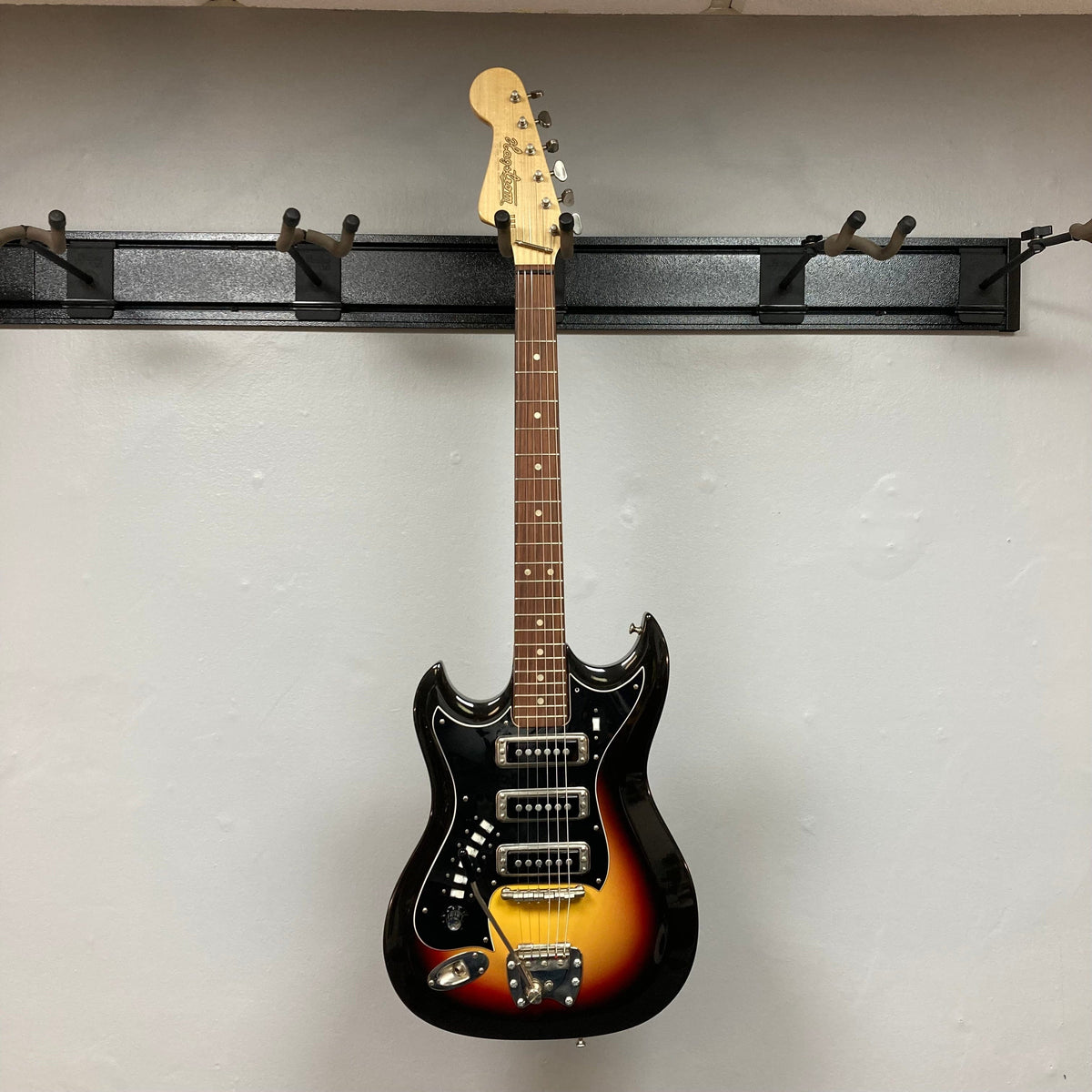 Hagstrom III Left Hand 1960s Sunburst Electric Guitar hanging on a wall, showcasing its vintage-inspired design and three single-coil pickups.