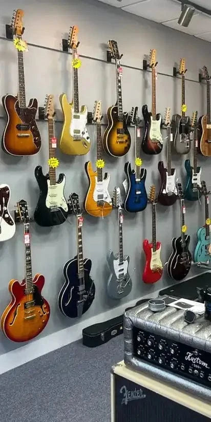 Wall displaying various guitars with a Fender amplifier in the foreground. Wall displaying various guitars with a Fender amplifier in the foreground.
