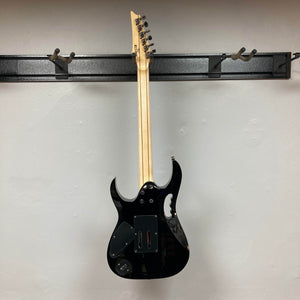 A black Ibanez JEM77P Steve Vai Signature by Guitars on Main hangs by its neck on a wall-mounted rack, viewed from the back against a plain light-colored wall.