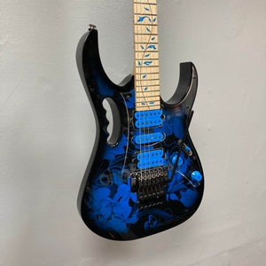The Ibanez JEM77P Steve Vai Signature by Guitars on Main features a black body with blue floral patterns, blue pickups, and a maple neck, displayed mounted on a light gray wall.